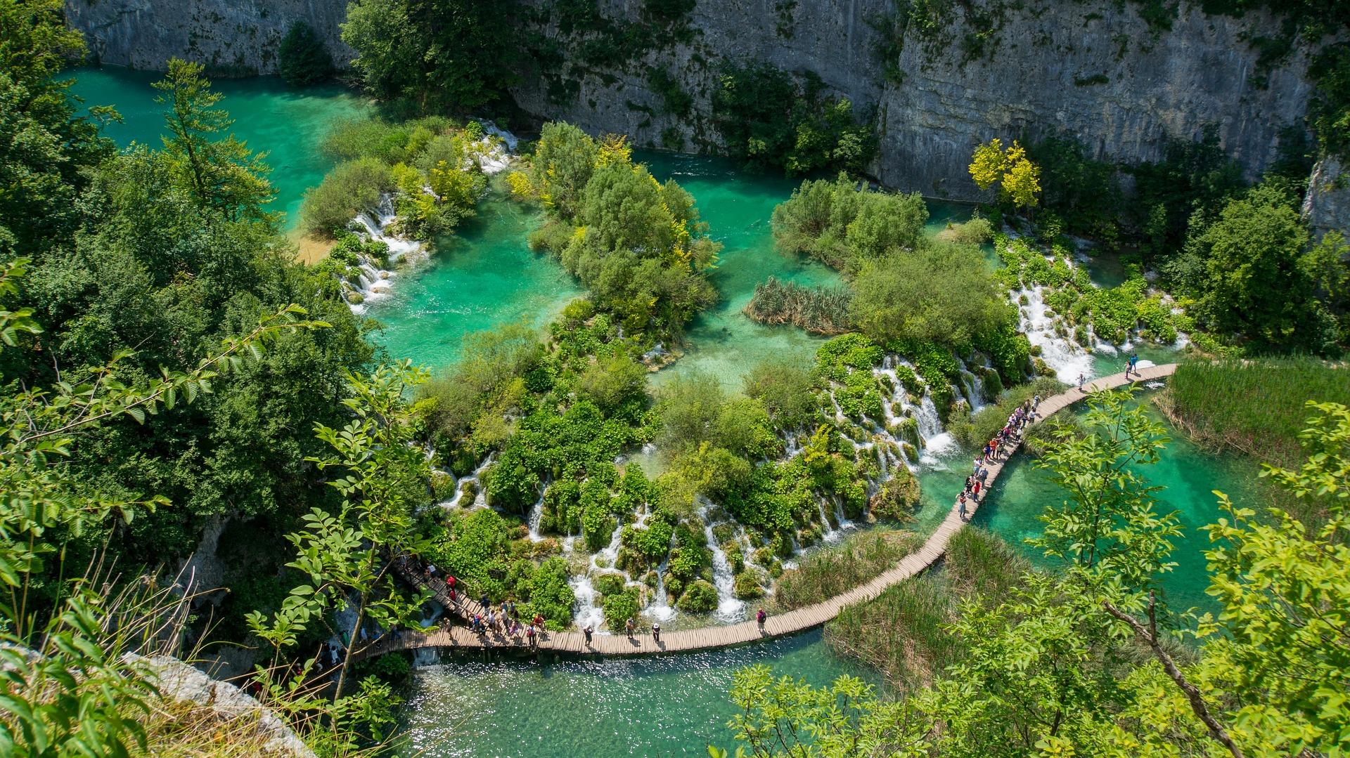 Plitvice waterfalls from bird perspective. Greenish blue lakes blended with green trees and a path for hiking in the middle.