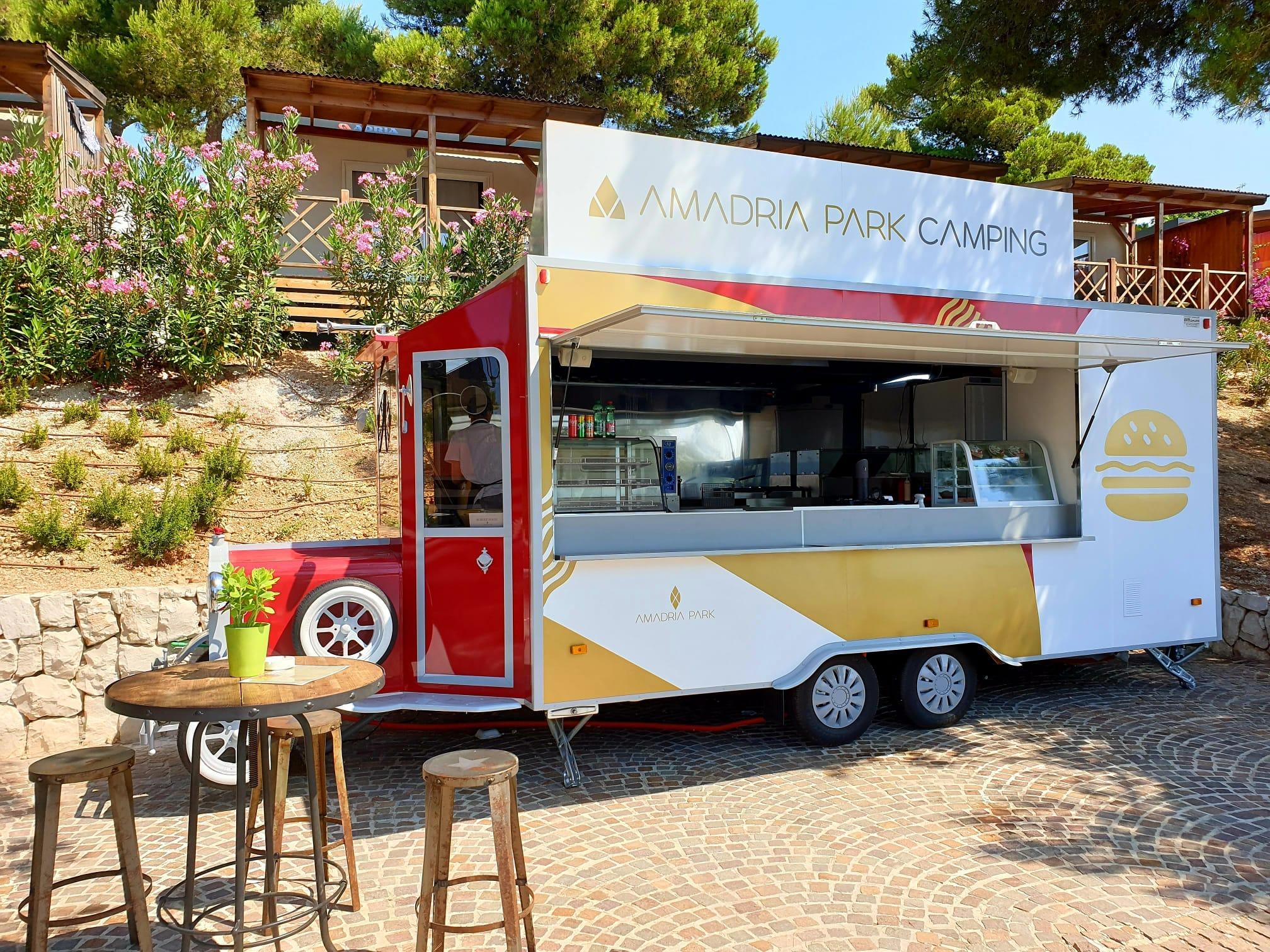 Mobile food stand in pine forest underneath wooden mobile homes with a small round wooden table in front.